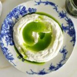 Basil oil poured over labneh in a blue dish