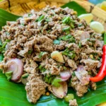 Thai beef larb salad with fresh shallots, herbs, and chili served on a banana leaf.