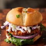 BBQ lentil burger in a bun with lettuce, tomato, onion, and slaw