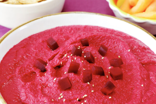 Closeup of bowl of red beet hummus sprinkled with beet cubes and sesame seeds