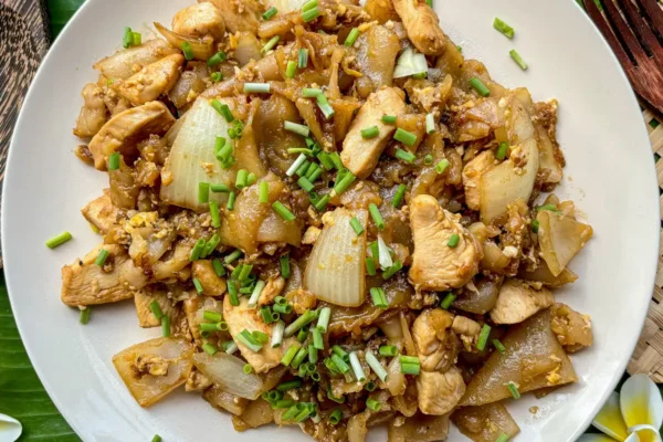 Best Daya Gaaa G Repeath pipe (Fords of Noodles) Overhead view of kuay teow kua gai stir-fry with tender chicken, wide noodles, and green onion on a white plate.