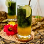 Green Thai tea with lime and honey, served in a tall glass with metal straw and garnished with a lime slice.