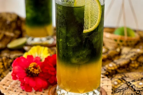 Green Thai tea with lime and honey, served in a tall glass with metal straw and garnished with a lime slice.