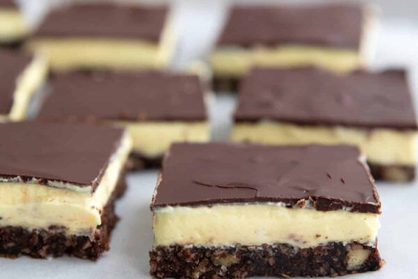 Keto Nanaimo Bars – All Day I Dream About Food Keto Nanaimo bars arranged on white parchment over a rustic blue plate.