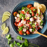 Ceviche in a blue bowl, beside lime wedges and cilantro