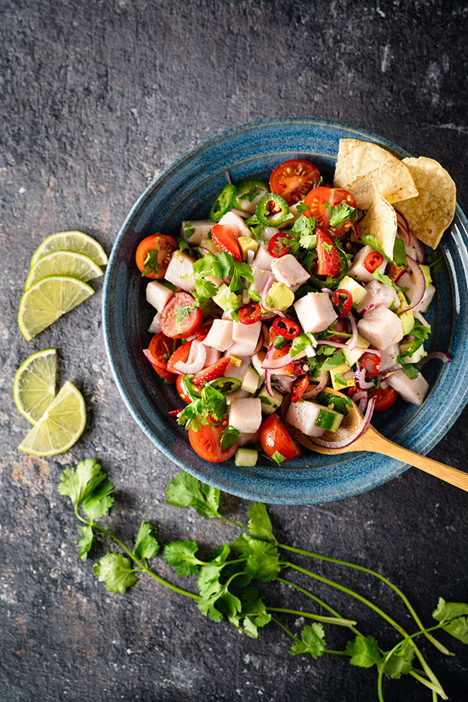 Ceviche in a blue bowl, beside lime wedges and cilantro