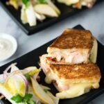 Two lobster grilled cheese sandwiches with salads on black plates