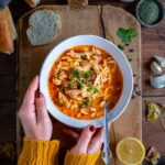Woman with a yellow jumper holding a bowl of Turkish chicken soup on a wooden board.