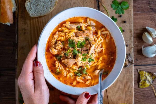 Woman with a yellow jumper holding a bowl of Turkish chicken soup on a wooden board.