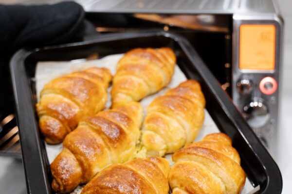 Hands in gloves holding up a tray of croissants in front of the air fryer