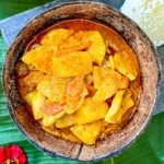 Thai gang garee curry featuring tender chicken and potatoes in a coconut shell.