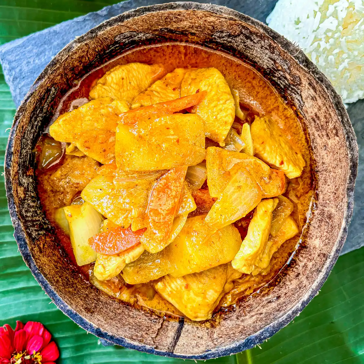 Thai gang garee curry featuring tender chicken and potatoes in a coconut shell.