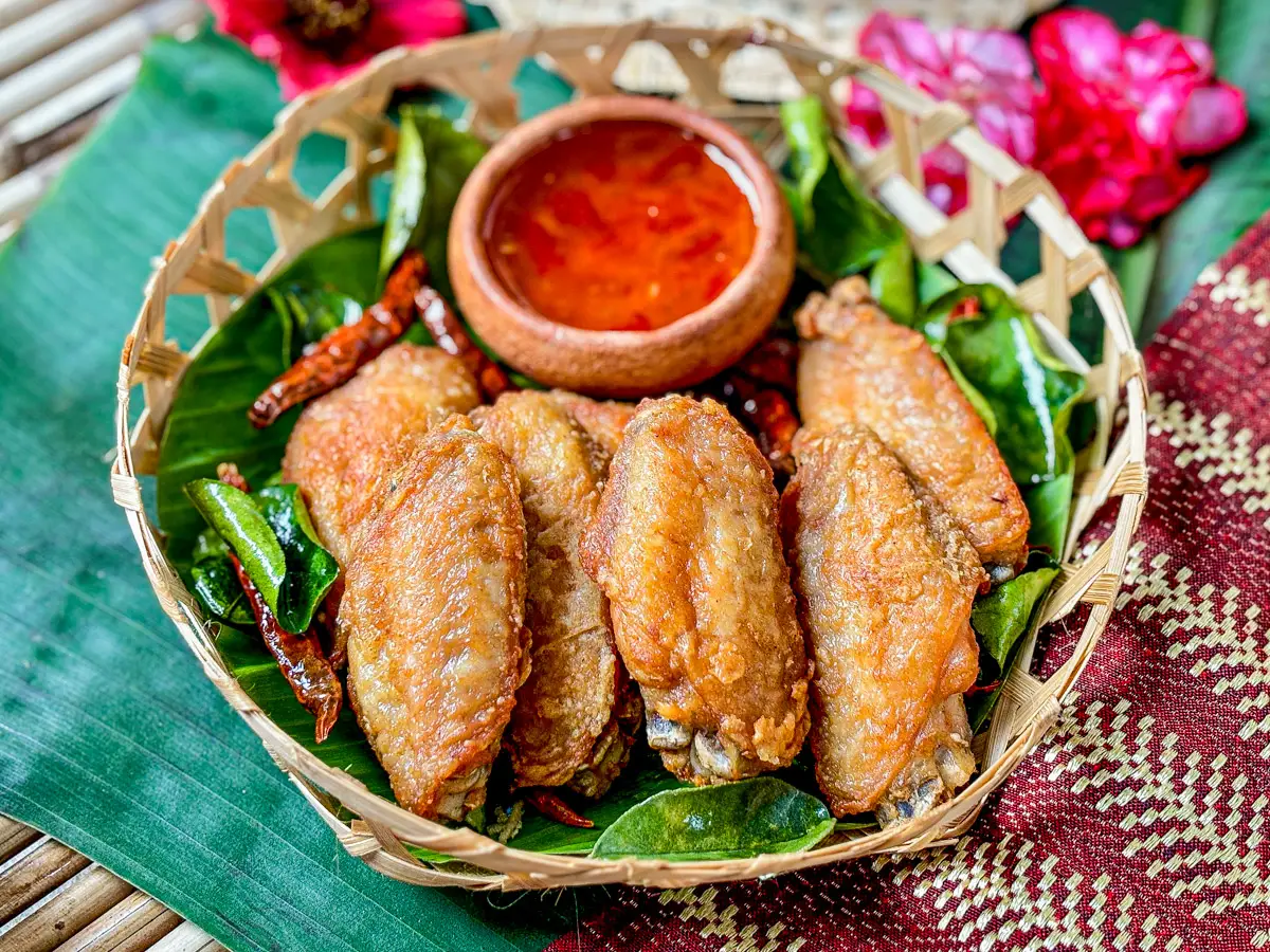 Kai tod, Thai fried chicken wings, in a traditional bamboo basket with sweet chili sauce.
