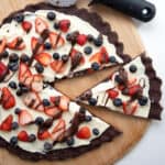 Top down image of Keto Chocolate Cookie Pizza on a wooden cutting board with a pizza cutter.