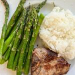lamb loin chops plated with rice and roasted asparagus on a white plate