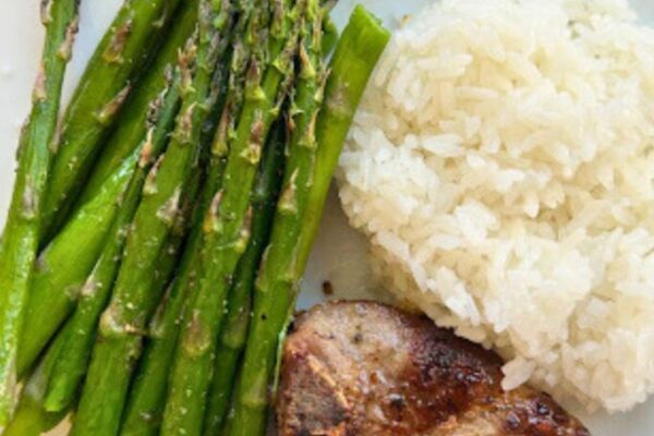 lamb loin chops plated with rice and roasted asparagus on a white plate