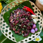 Thai raw beef larb salad served on banana leaf with chili, garlic, and shallots in a woven bamboo tray.