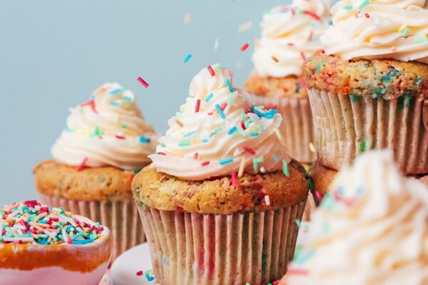 Sprinkling rainbow sprinkles over a batch of frosted funfetti cupcakes