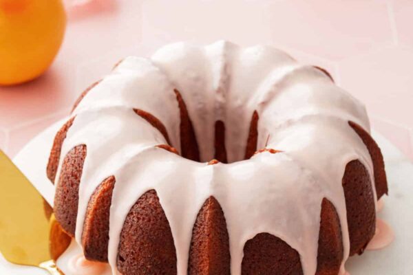 Pink glazed grapefruit bundt cake on a marble cake plate with a pink background and a cut pink grapefruit in the background.