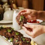 Greek Burger on a plater with hands holding a patty