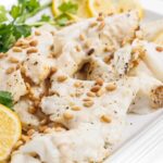 Close up view of grilled white fish with tahini lemon sauce and garnished with toasted pine nuts.