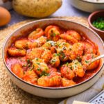 bowl of gnocchi covered in red sauce on counter with things around.
