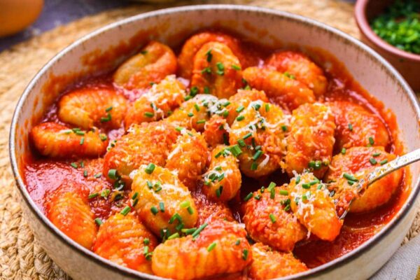 bowl of gnocchi covered in red sauce on counter with things around.