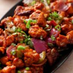 Side image of indo chinese spicy chicken served in a an oval black platter.