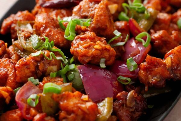 Side image of indo chinese spicy chicken served in a an oval black platter.