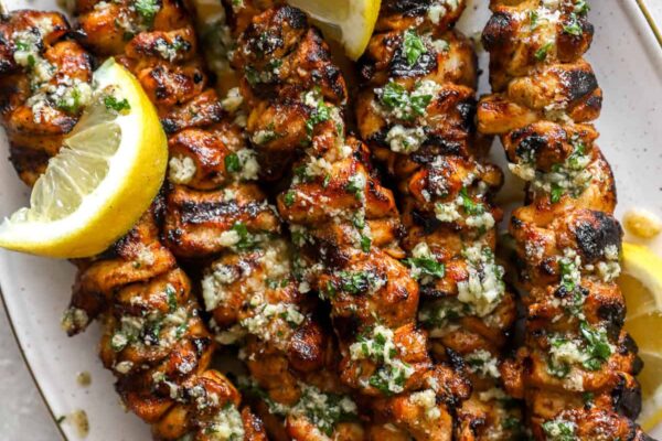 Lemon Garlic Parmesan Chicken Skewers A platter of lemon pepper Parmesan chicken skewers with lemon wedges.