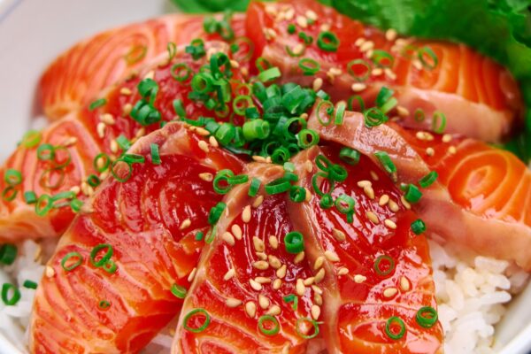 Marinated Salmon Sashimi Donburi Close-up of a donburi bowl bursting with glossy salmon zuke, sprinkled with sesame and scallions, nestled against vibrant green shiso leaves.