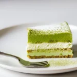 Slice of matcha tiramisu dusted with matcha powder on a white plate.