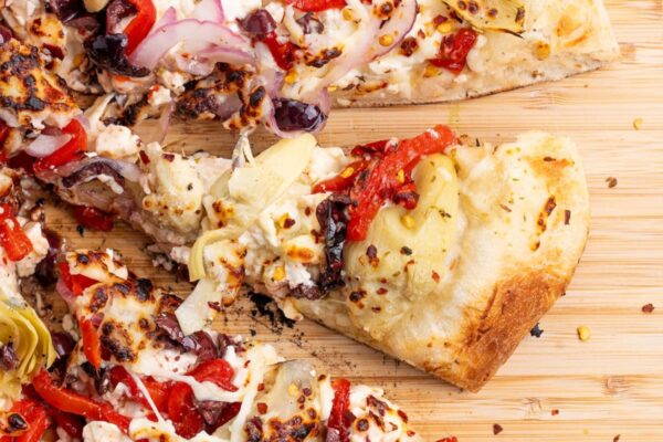 Four slices of Mediterranean veggie pizza on a cutting board.