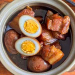 Thai moo palo with braised pork belly and soy-stewed eggs in a clay pot, showing glossy skin and rich, dark broth.