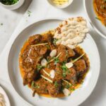 Lamb Korma on a plate garnished with blanched almonds, cilantro, and julienned ginger