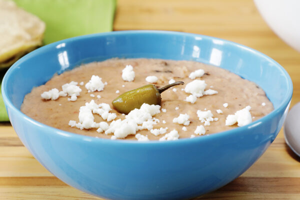 Mexican pork beans in blue bowl garnished with grated cheese and a whole jalapeño