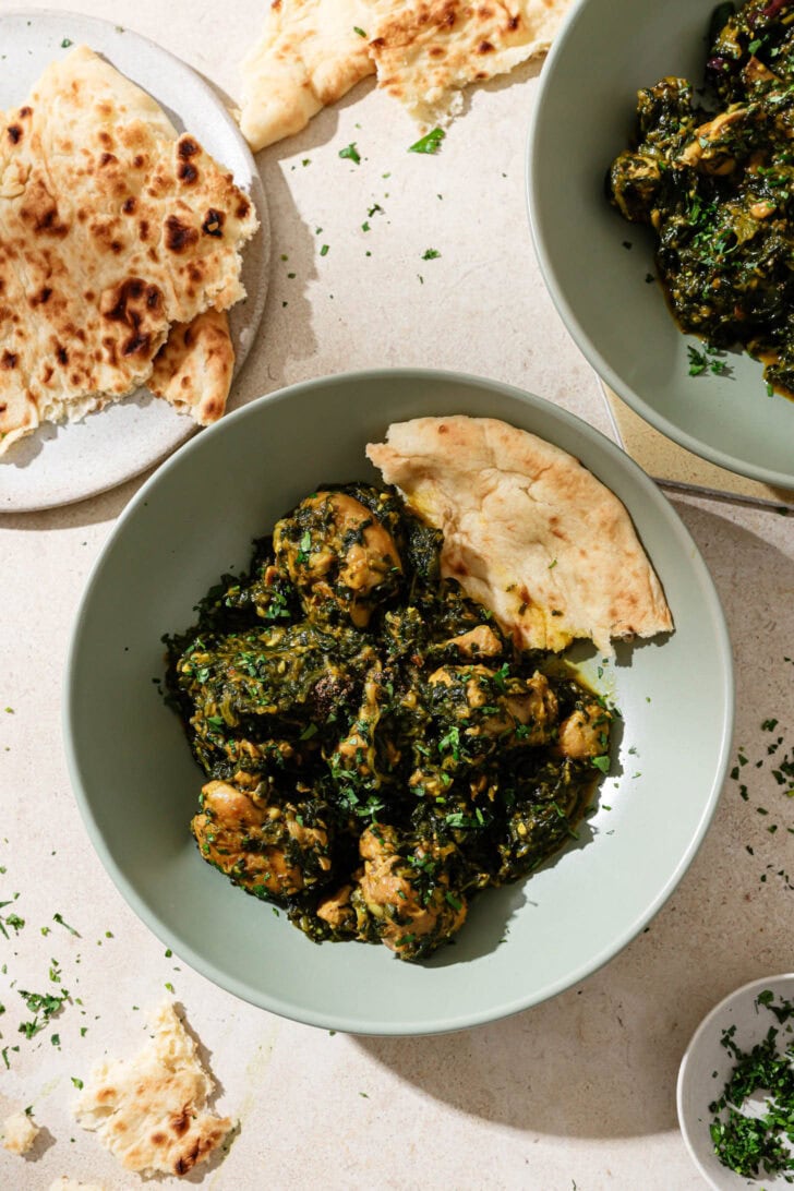 A blue bowl with Palak Chicken and naan ready to be eaten.