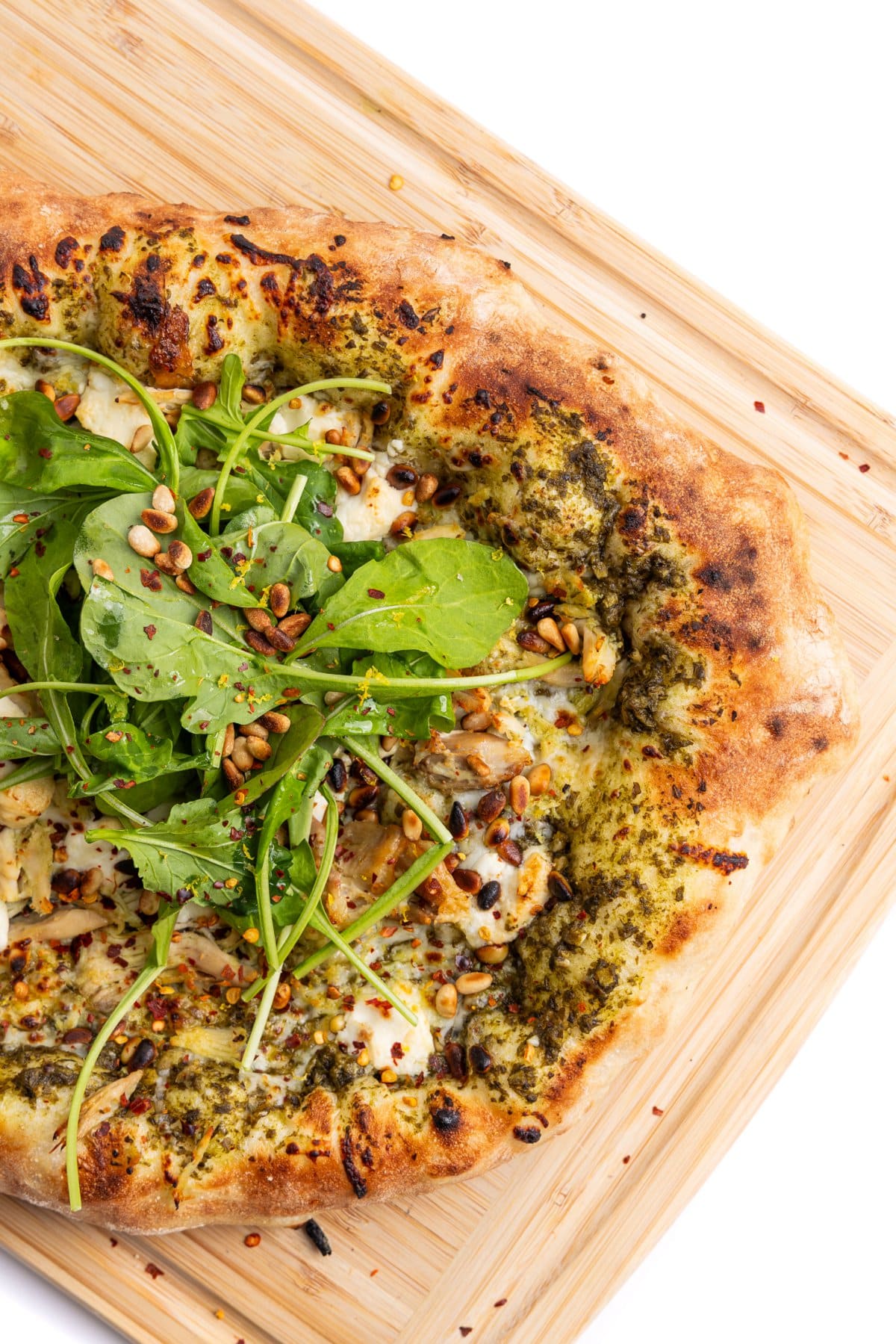 Pesto chicken pizza with goat cheese and pine nuts topped with arugula on a cutting board.