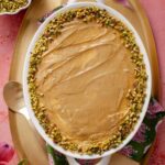 Oval dish filled with creamy pistachio tiramisu, topped with chopped pistachios around the edge, placed on a golden tray with a floral napkin.