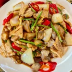 Pork with oyster sauce stir-fry with mushrooms, onion, red chilies, and green onion on a white plate.