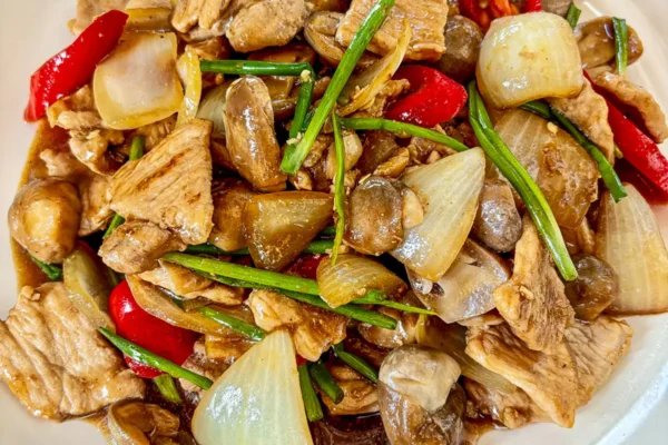 Pork with oyster sauce stir-fry with mushrooms, onion, red chilies, and green onion on a white plate.