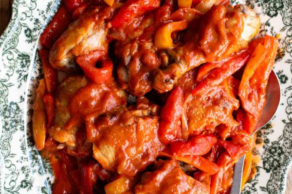 Italian chicken and peppers in a tomato sauce on a large platter serving plate on a rustic wooden surface.