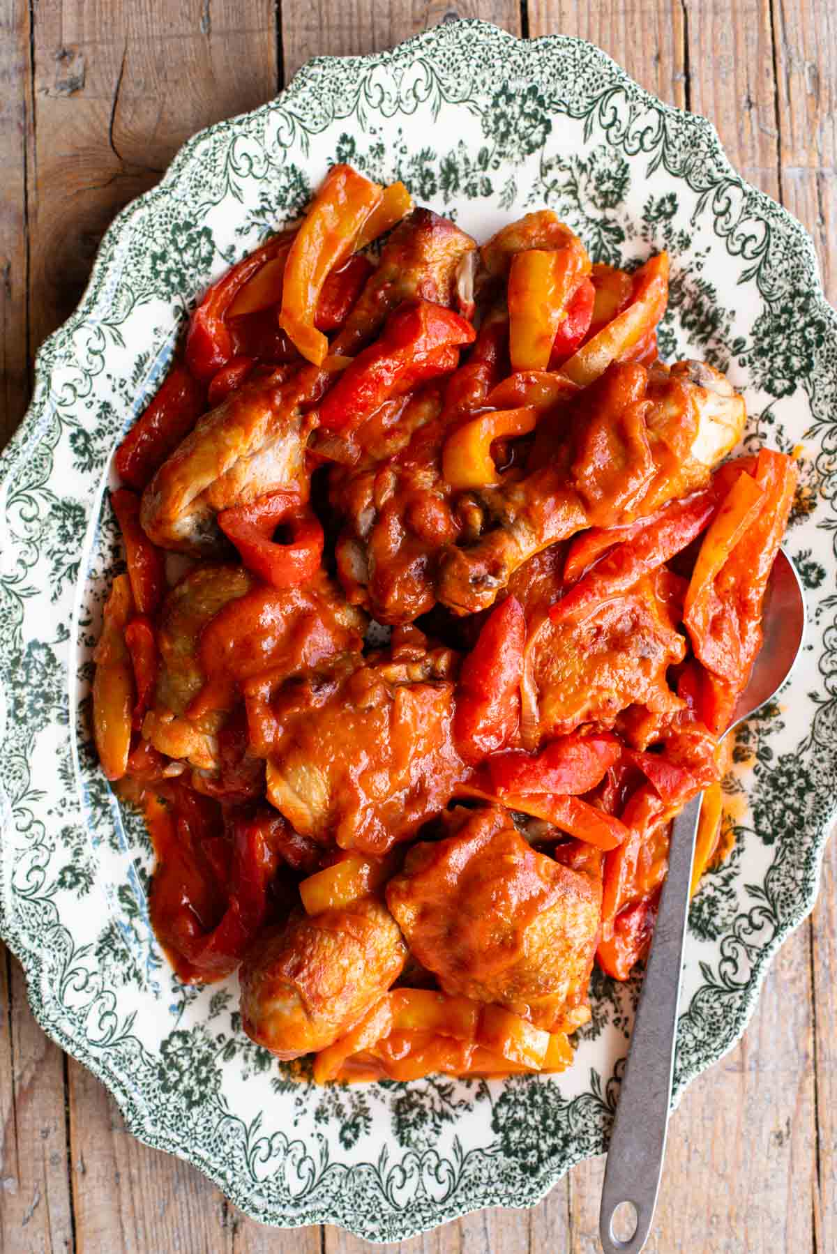 Italian chicken and peppers in a tomato sauce on a large platter serving plate on a rustic wooden surface.