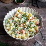 Russian salad in a white bowl and a spoon inside it.