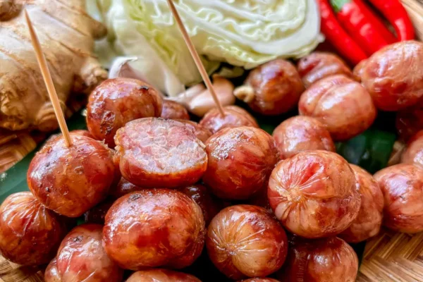 Sai Krok Isan (Thai Sausage Recipe) Sai krok Isan Thai sausages on a bamboo basket, with a backdrop of chilies, ginger, and cabbage.