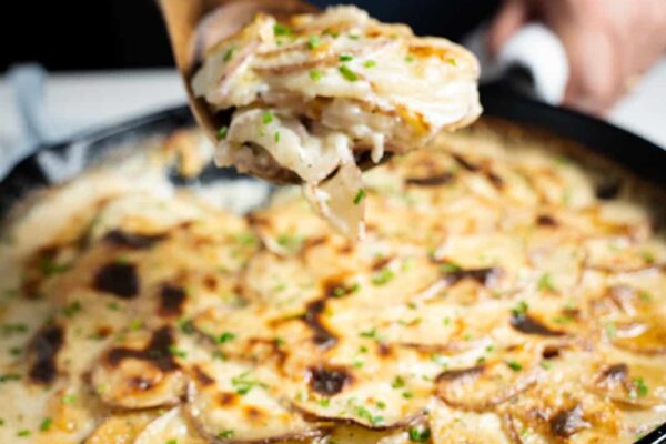 Scalloped potatoes in a cast iron pan Up close picture of scalloped potatoes in a cast iron pan and a hand holding up a spoon-full of potatoes.