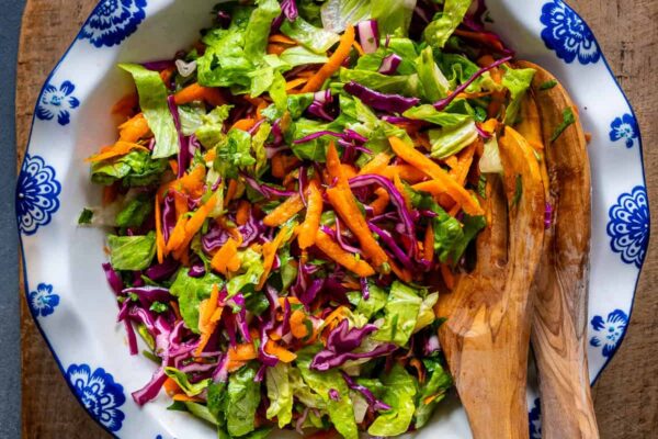A fresh salad with lettuce, carrots and red cabbage in a white bowl and wooden spoons inside it.