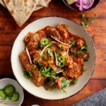 Kadai goat served in a beige bowl and garnished with cilantro and ginger.