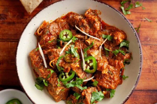 Kadai goat served in a beige bowl and garnished with cilantro and ginger.