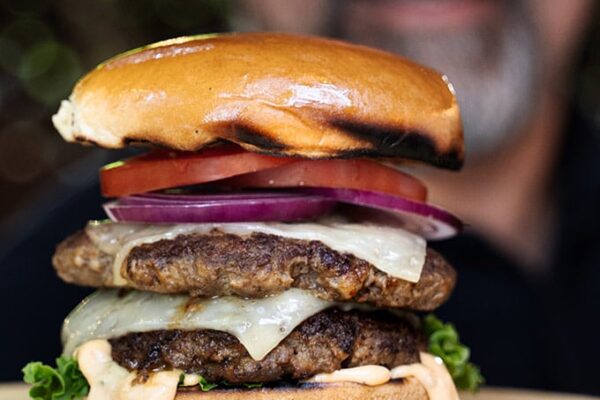 Smashed burgers on cast iron Me holding up a fully assembled burger on a wood plate